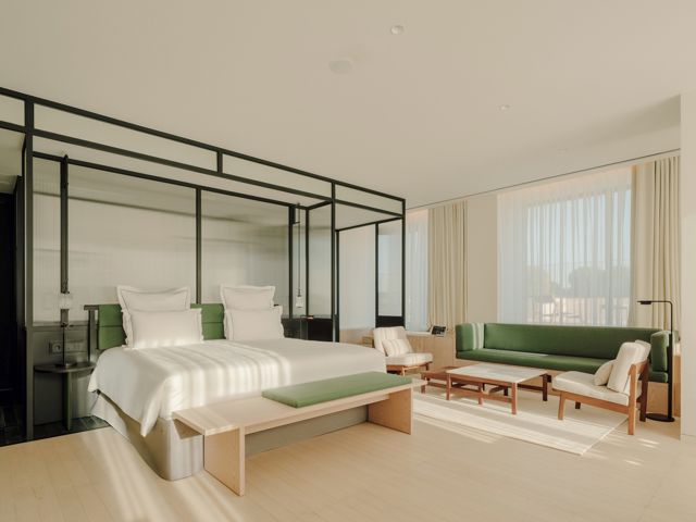 Interior of the Grand Terrace Club Suite designed by Neri & Hu, showcasing a blend of Brutalist architecture with warm wood accents, a king-sized bed, and an outdoor terrace with a view of Republic Square